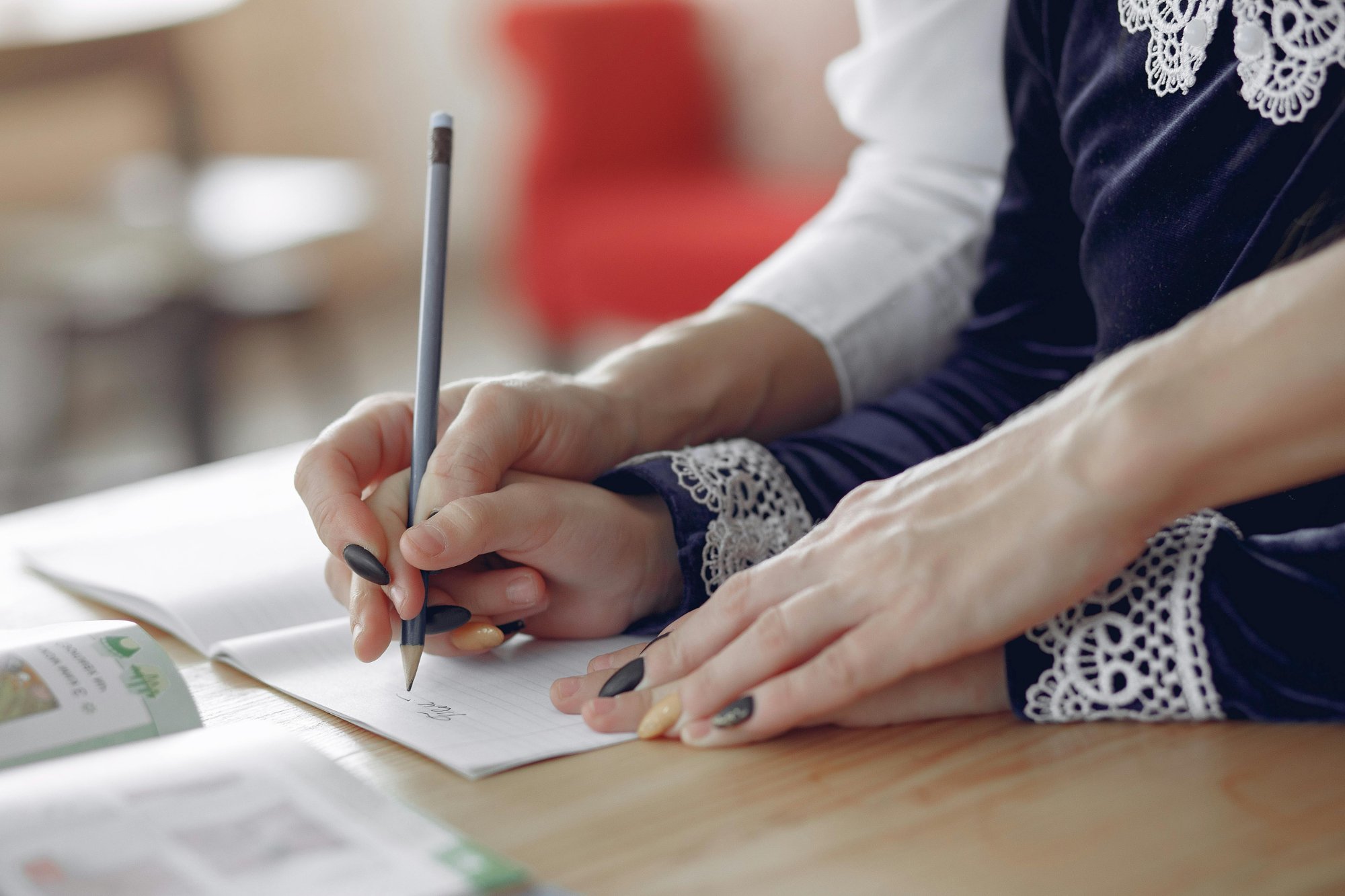 child writing at desk with tutor